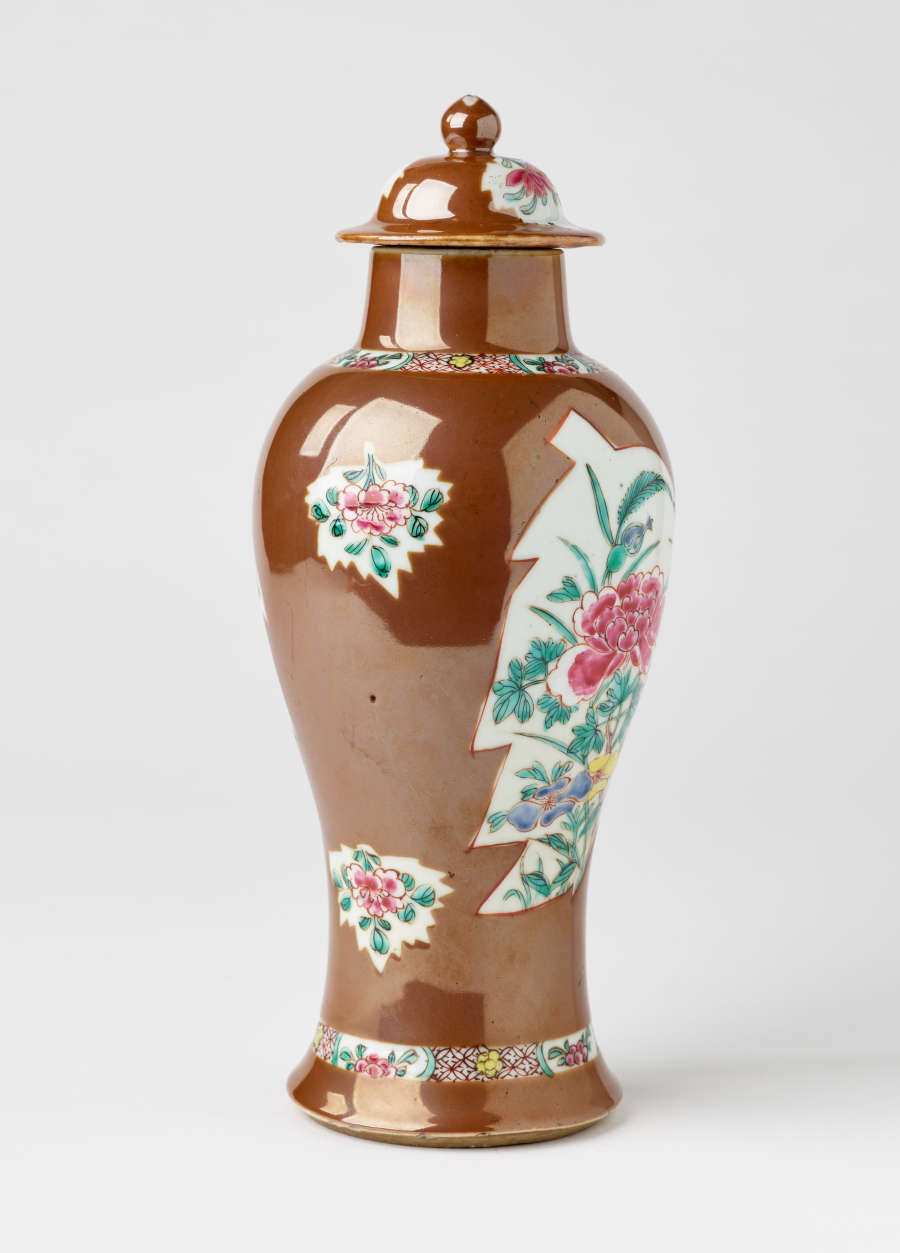 A brown and white covered vase with pink, green, blue, and yellow floral decorations.