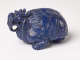 A side view of a blue sculpture of a horned tortoise, whose surface is covered with carved geometric patterns.