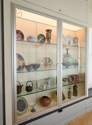 A case with four shelves is set into a wall. The shelves hold many different ceramic objects.