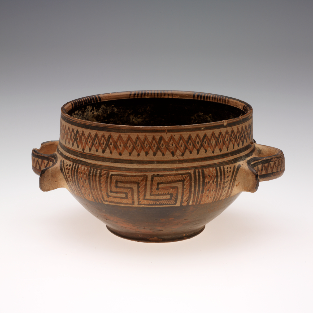 A round, two-handled ceramic earthenware bowl with a dark interior, dark lower half, and upper band decorated with intricate tan and brown geometric patterns around the rim. 