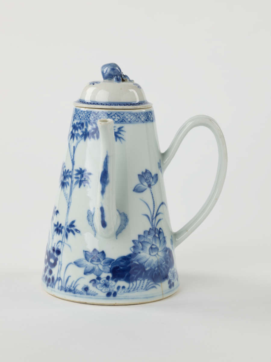 A white and blue teapot with floral decorations, a lid with a small semi spherical finial, spout, and a handle which is located approximately 90 degrees from the spout.