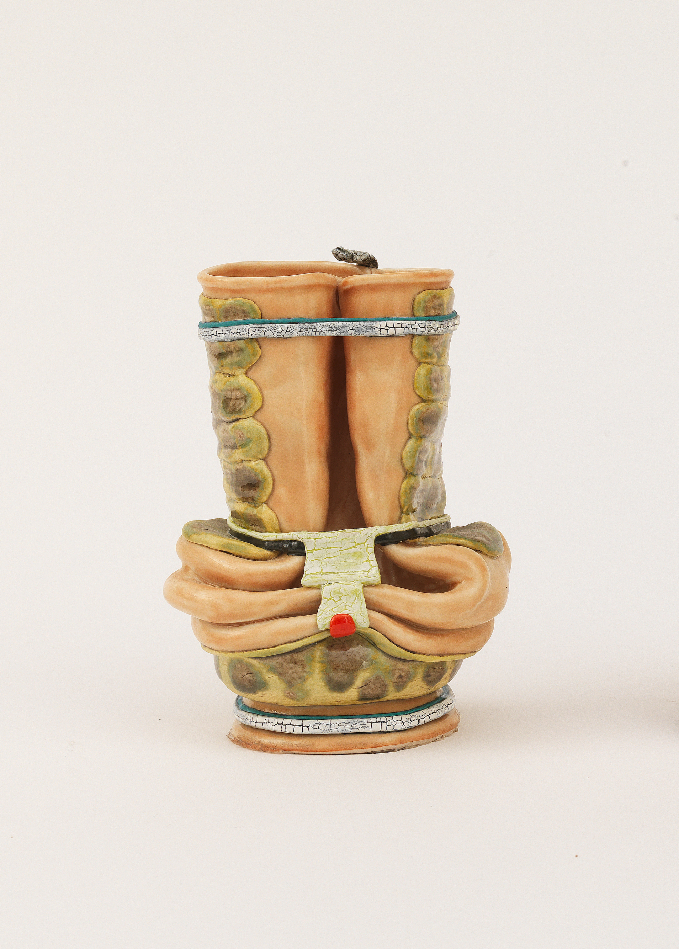 A small ceramic vessel of intertwined hands gripping a scroll decorated with green patterning resembling snake skin and a tiny snake resting on the top rim. 