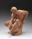 Terracotta statue depicting a realistically carved, muscular bearded man sitting, his body tense as he holds a rounded vessel with a creatures face between his legs.