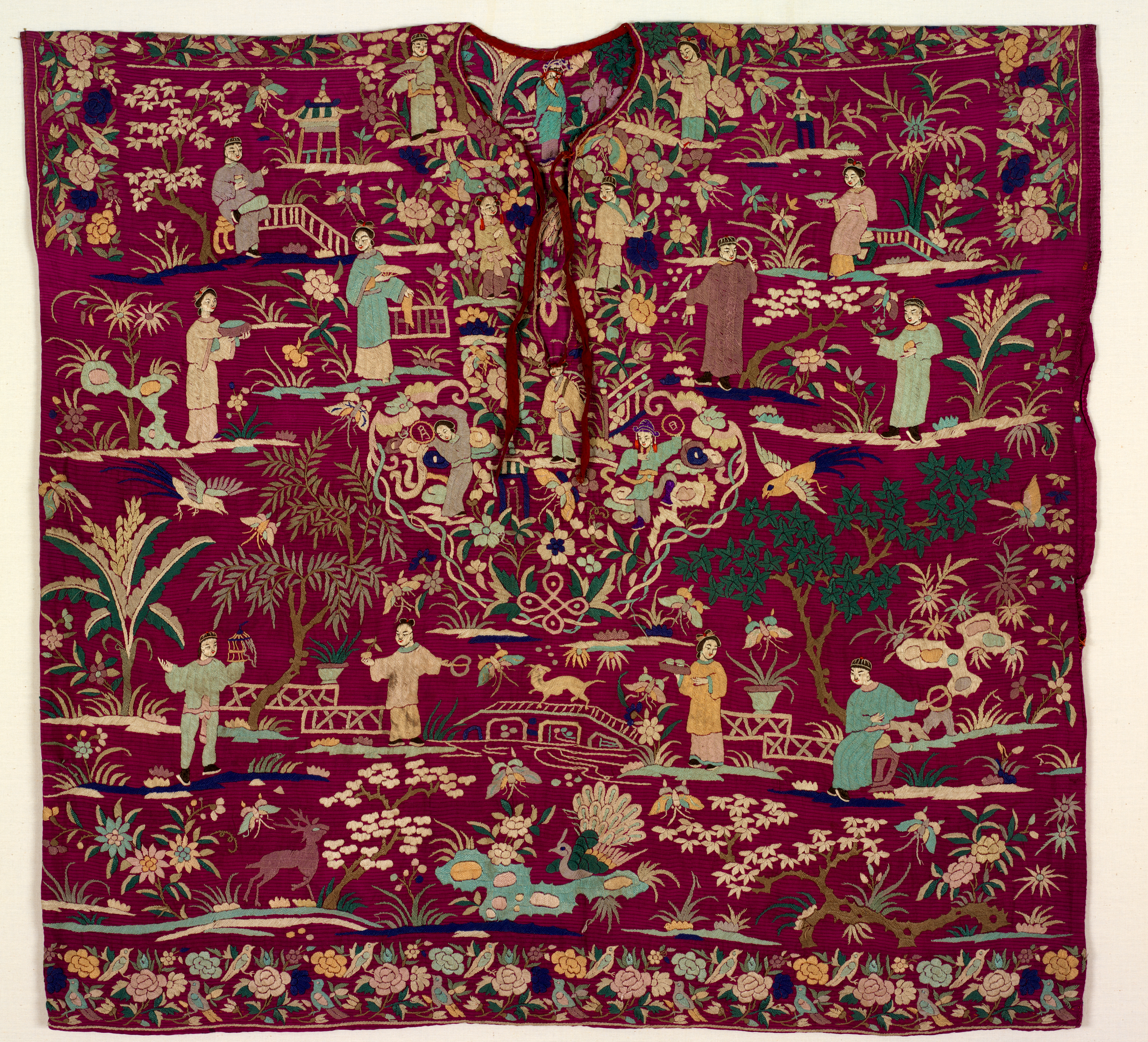 A richly embroidered tunic with intricate depictions of figures, birds, plants, and bridges in vibrant colors on a red background.