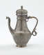 A silver coffee pot with detailed delicate decorations, handle with a lid hinged to it, and spout.