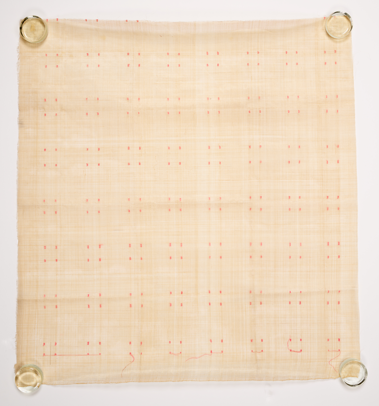 Beige square of woven fabric on a light background which is held at the corners by clear fasteners. The surface features a subtle grid of repeated pink dots.
