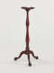 A tall, wooden candle stand with turned legs and ornate, tripod feet.