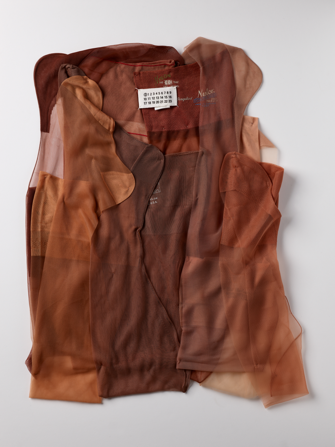 Layered sheer fabric in various brown tones laid flat, with a design label reading "Maison Margiela".