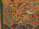 An embroidered yellow deer-like animal with blue hooves, horse-like tail, and red wings surrounded by smoke-like clouds and a snake floating above navy waves against gold and green fabric. 