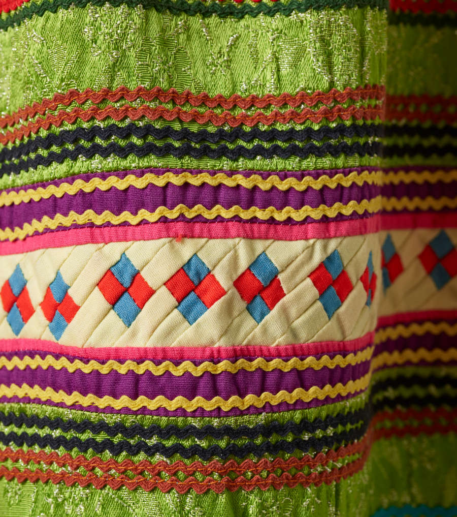 Another detail of the pattern. A thick strip of off-white with red and blue squares woven through it is surrounded by wavy horizontal orange, black, purple, pink, and yellow stripes. 