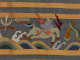 Detail of an intricately embroidered scene depicting a hoofed mythical beast colored light blue galloping above ocean waves, surrounded by abstract curving and flame motifs and framed by gold stripes.