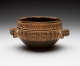A round, two-handled ceramic earthenware bowl with a dark lower half and upper band decorated with intricate tan and brown geometric designs.