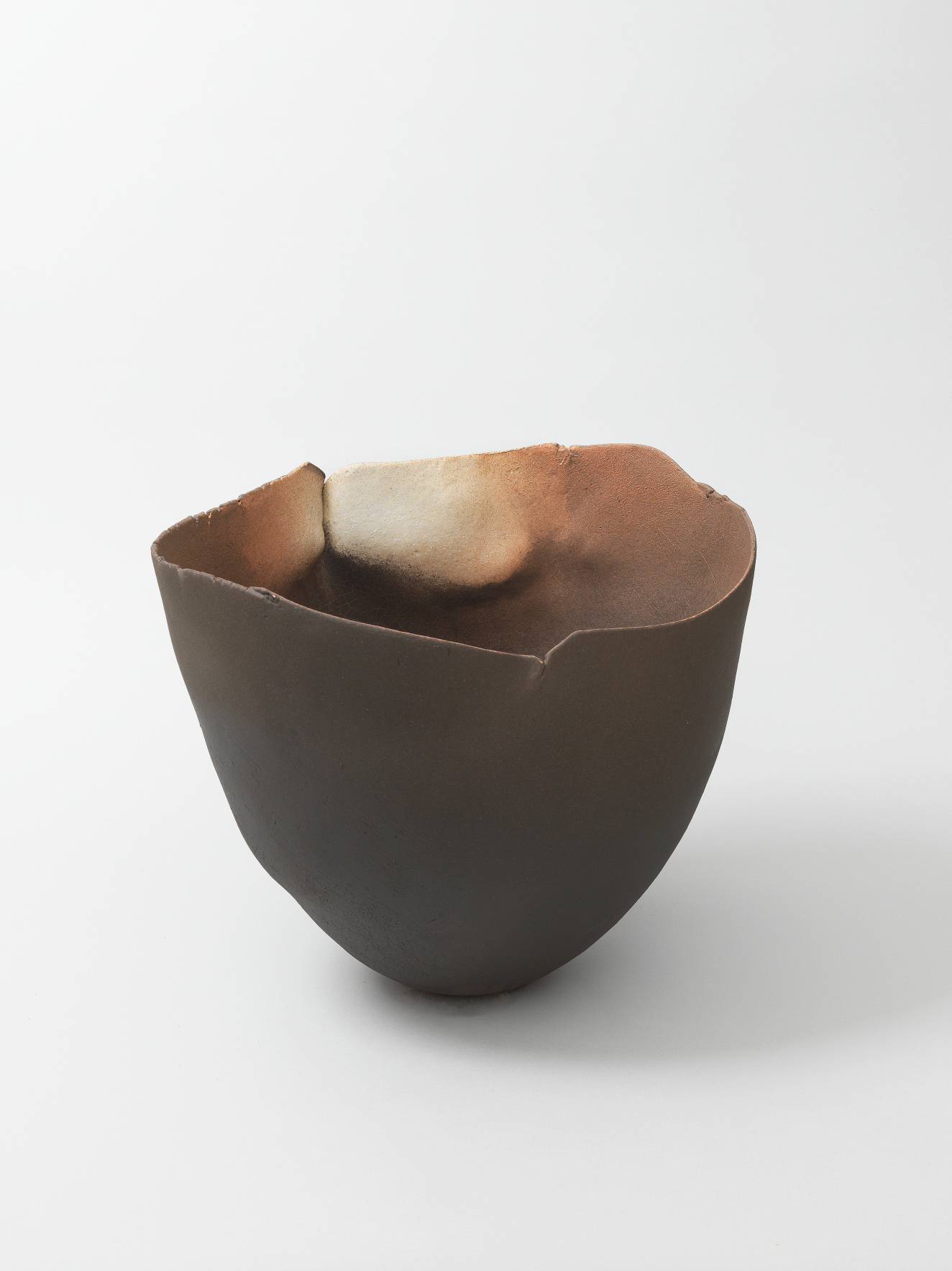 Hand-shaped dark ceramic bowl with a thin, uneven rim and softly rounded body, its smoky interior blending soft shades of cream, brown and black.