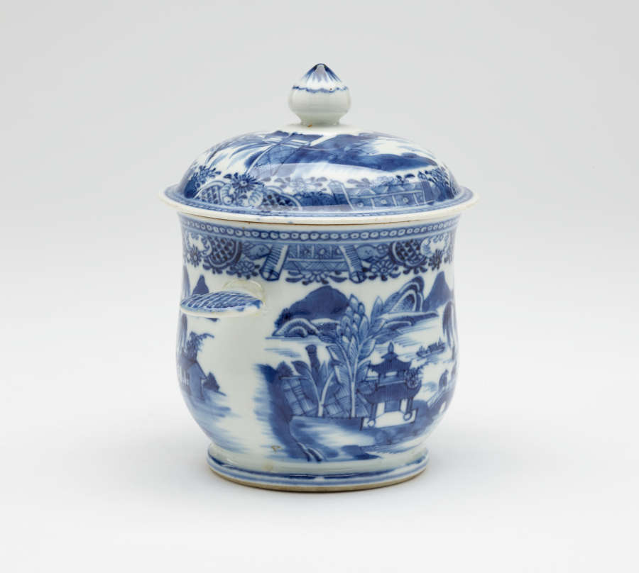 A white bowl with flat handles and lid. The blue decorations are architectural and floral.