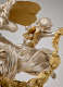 Back view of a detailed silver cherub with small gold wings, one arm grasping a gold leaf garland while perched upon a larger winged, robed figure decorated with stars. 