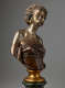Bronze bust of a woman with raised chin, hair in twists, gold earrings, beaded necklaces, and shoulders exposed in a strapless wrapped dark top mounted on a gold base.