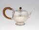 A bulbous silver teapot with a wooden finial and handle connected with decorative silver pieces. There are delicate engraved marks on the body and lid.