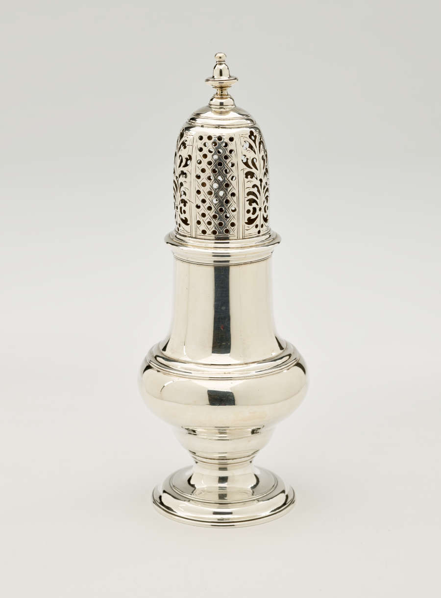 A silver vessel with a foot, rounded body that goes to a cylindrical top half, and the lid is perforated with small holes and floral cutouts.