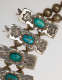 Detail-view of ornaments threaded into the necklace’s beaded chain. The rectangular ornaments have turquoise stones set in their center with silver decorative engraved borders on either side.