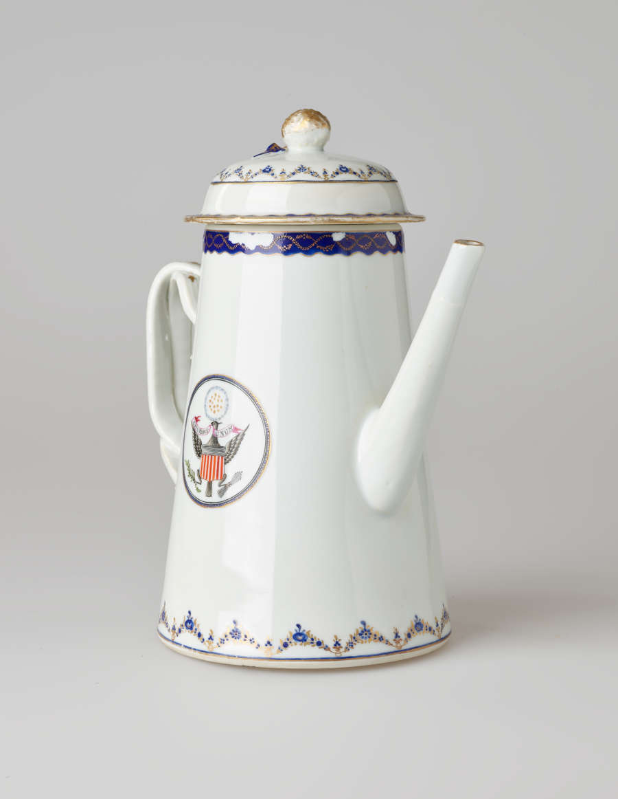 A white coffee pot with dark blue and gilded decorations, a straight spout, angular handle, and heraldry imagery in a circle on the body of the coffee pot.