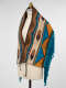 Side view of a mannequin wearing a multicolored woven fabric with fringe and tassels. 
The woven fabric contains brown feather motifs in between chevron designs and turquoise and yellow triangles. 