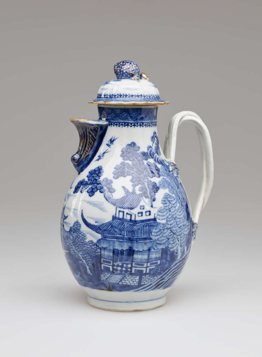 A white and blue chocolate pot with a spout, handle, and lid, the edges of the lid and spout are gilded. The decorations mainly depict floral, architectural, and landscape elements.