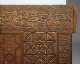 A close-up of a carved wooden panel featuring intricate calligraphy along the top edge, geometric star patterns and detailed floral patterns along the right edge. 