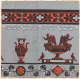 Aged, gray wallpaper with orange and black floral borders, and two vases in the center, one with birds as handles and the other with winged women sitting on its mouth.