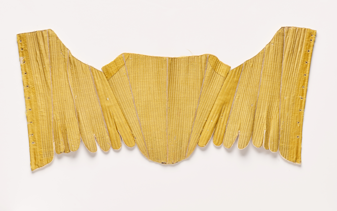  Photo of an intricate gold-colored sewn form, lying flat. The center panel is roughly triangular. The symmetrical side panels have rounded edges at the bottom.