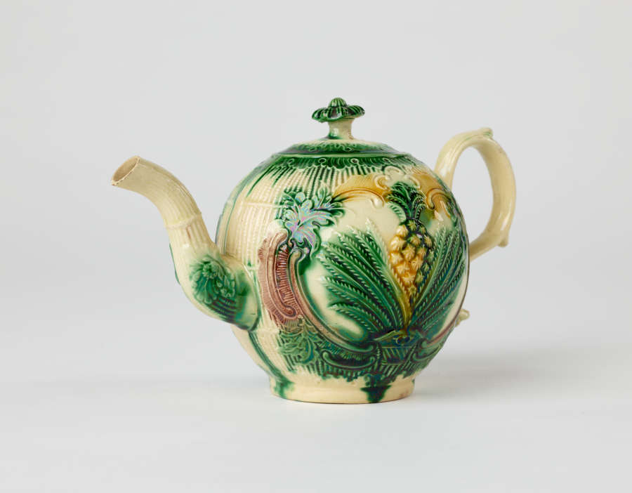 A bulbous teapot with white, green, and yellow floral decorations in the form of a leafy pineapple.