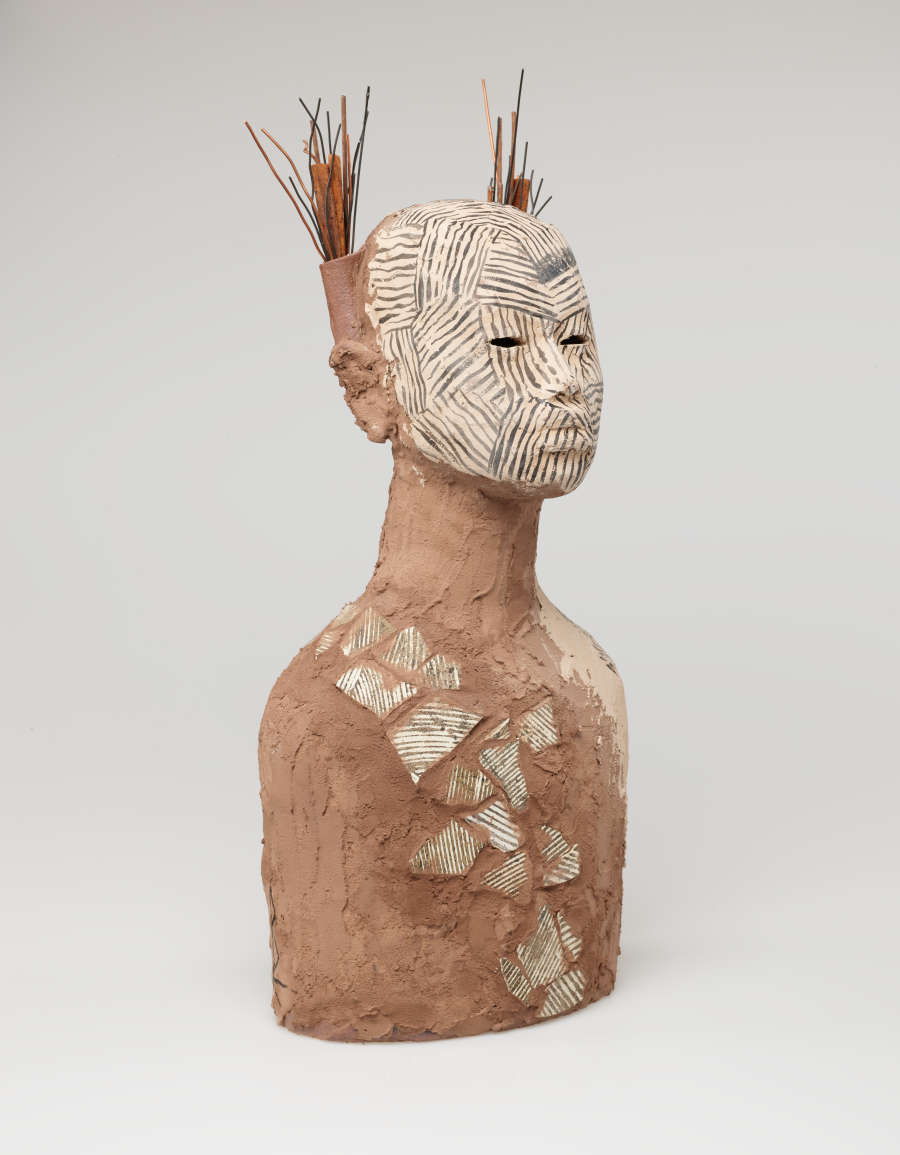 Side view of the bust, revealing that the headdress is composed of a bundle of sticks rising from behind the head. The sticks are placed into a narrow vessel attached to the head. 
