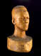 Three quarter front view of a wooden bust depicting the head of a male figure with afrocentric facial features. His expression is stern and holds an intense gaze.