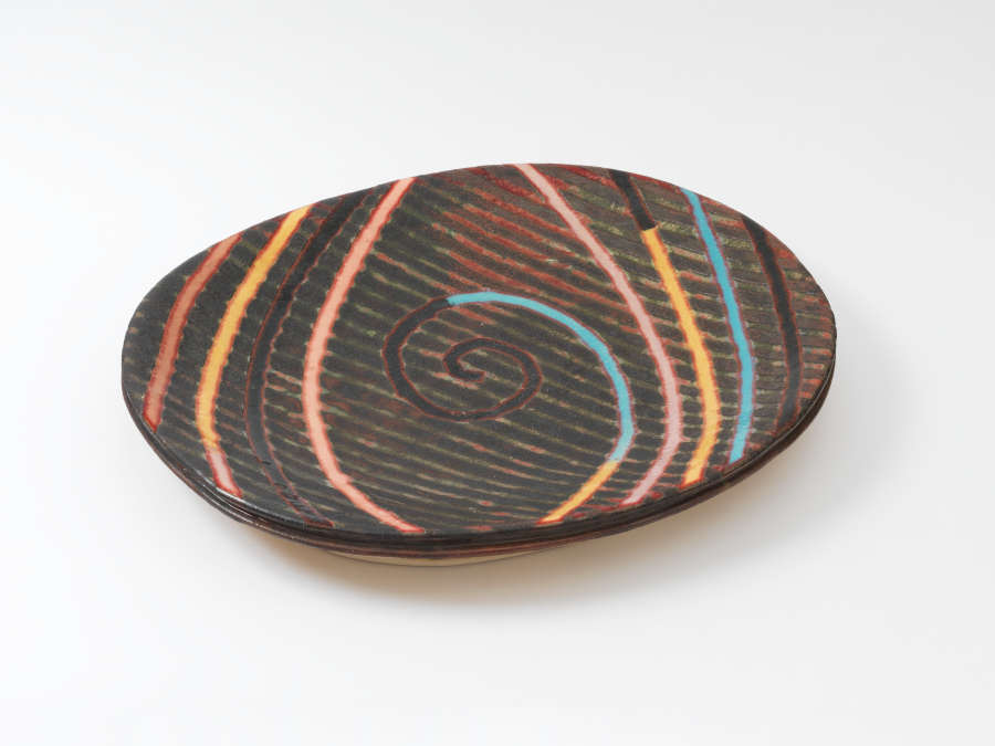 An oval, and shallow brown platter with vertical, woodgrain-like patterning overlaid with brightly colored spirals and lines in pink, yellow and turquoise.