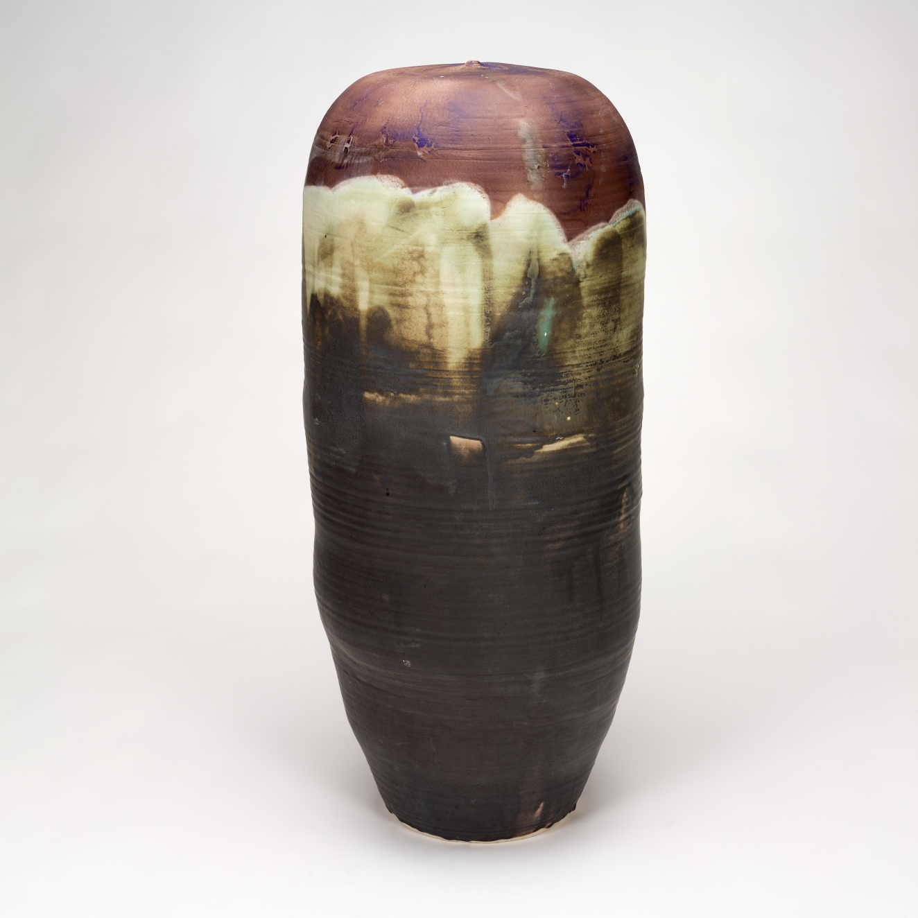 Tall and organic porcelain form with dark earth tones with a cream glaze dripping from the top. Cool blue and purple smudges tint the top area.