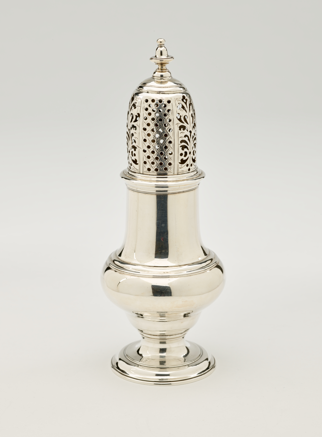A silver vessel with a foot, rounded body that goes to a cylindrical top half, and the lid is perforated with small holes and floral cutouts.