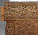 A close up of a carved wooden panel with calligraphic inscriptions along the top and interlocked geometric floral designs.
