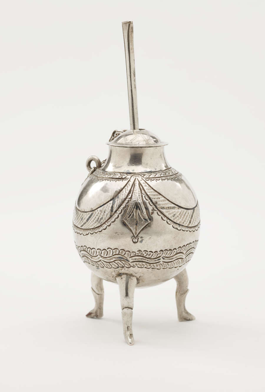 A silver covered jar and dipper that has long feet, a chain connecting the body and lid.