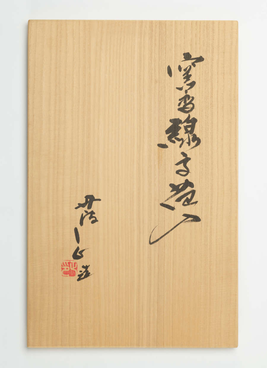 Tan rectangle with a wooden texture and black calligraphy arranged in two columns. The leftmost column features a red stamp at the bottom and is shorter than the right column.