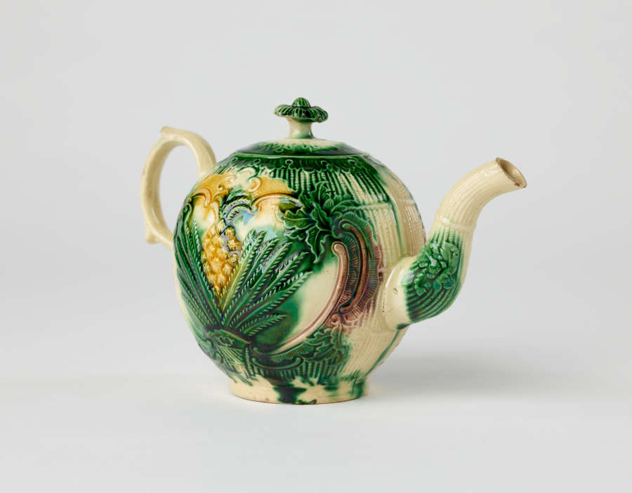 A bulbous teapot with white, green, and yellow floral decorations in the form of a leafy pineapple.