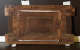 The back of a wooden panel with metal brackets and white straps, displaying signs of age and reinforcement.