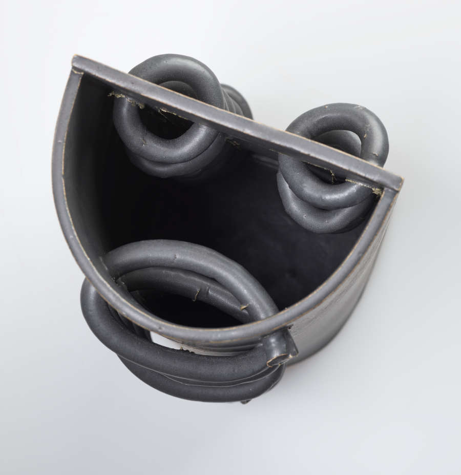  A top-down view of a circular, gray, open-top, ceramic sculpture. Interlaced loops are along two facing sides.