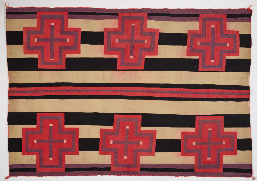 Black and cream striped woven blanket with six evenly spaced pink and purple bordered cross designs throughout. In the center there is a purple stripe in between two pink stripes. 