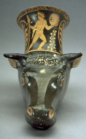 Black and terracotta cup with a sculpted cow’s head as its base, its top extending into the body of the cup, which is illustrated with men besides large floral motifs. 