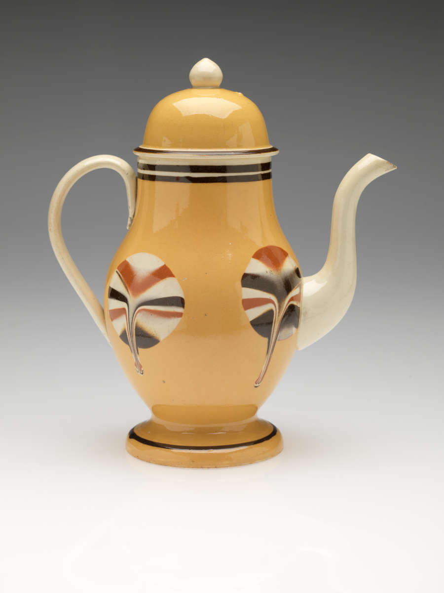 A yellow teapot with cream, orange, and brown circular designs dripping down at the bottom. Handle, spout, and final are cream colored.