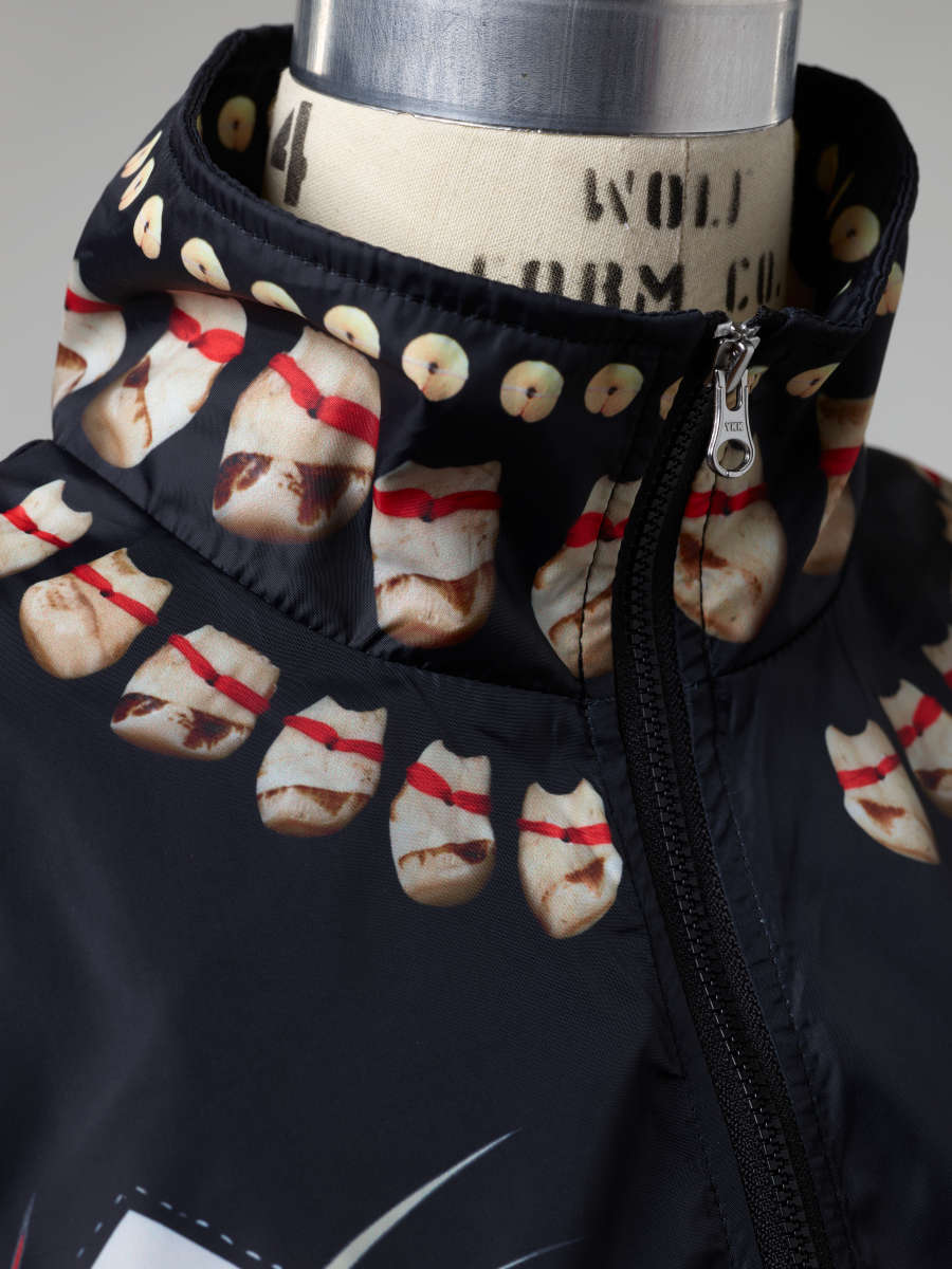 Detail of the windbreaker’s zippered collar, with a row of white circles going around the upper edge and two rows of tooth-like motifs with red stripes going around the neck.