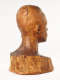 Three quarter back view of a glossy wooden bust depicting the head of a male figure. The wood features long vertical cracks, carving marks and color variation.