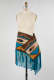 Turquoise, beige, and yellow geometric patterned woven fabric with fringe, wrapped around the hip of a mannequin. The turquoise fringed ends are the same length as the woven fabric. 