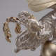 A silver cherub with gold wings, wavy hair, mouth open, and arms outstretched holds the end of a gold leafy garland, perched upon a larger silver-robed figure.