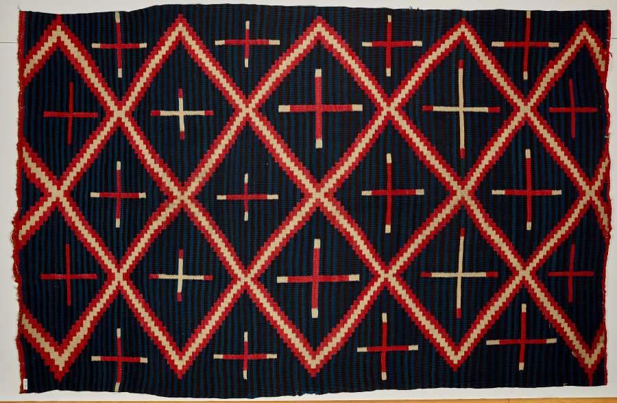 Striped navy blue blanket with three, different sized, alternating cross patterns: red crosses, red with white tips, and white with red tips, within a red and cream three-striped diamond pattern.