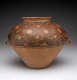 A large, rounded clay vessel with a narrow rim and two small handles,  decorated with red and black lattice.